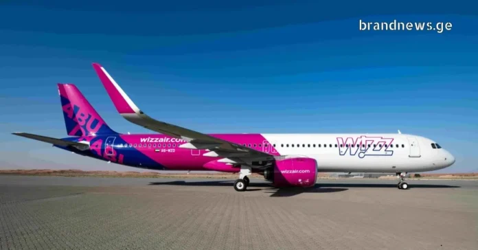 profile view of a Wizz Air Airbus A320 aircraft with its white, purple, and magenta livery, parked on the airport tarmac under a clear blue sky.